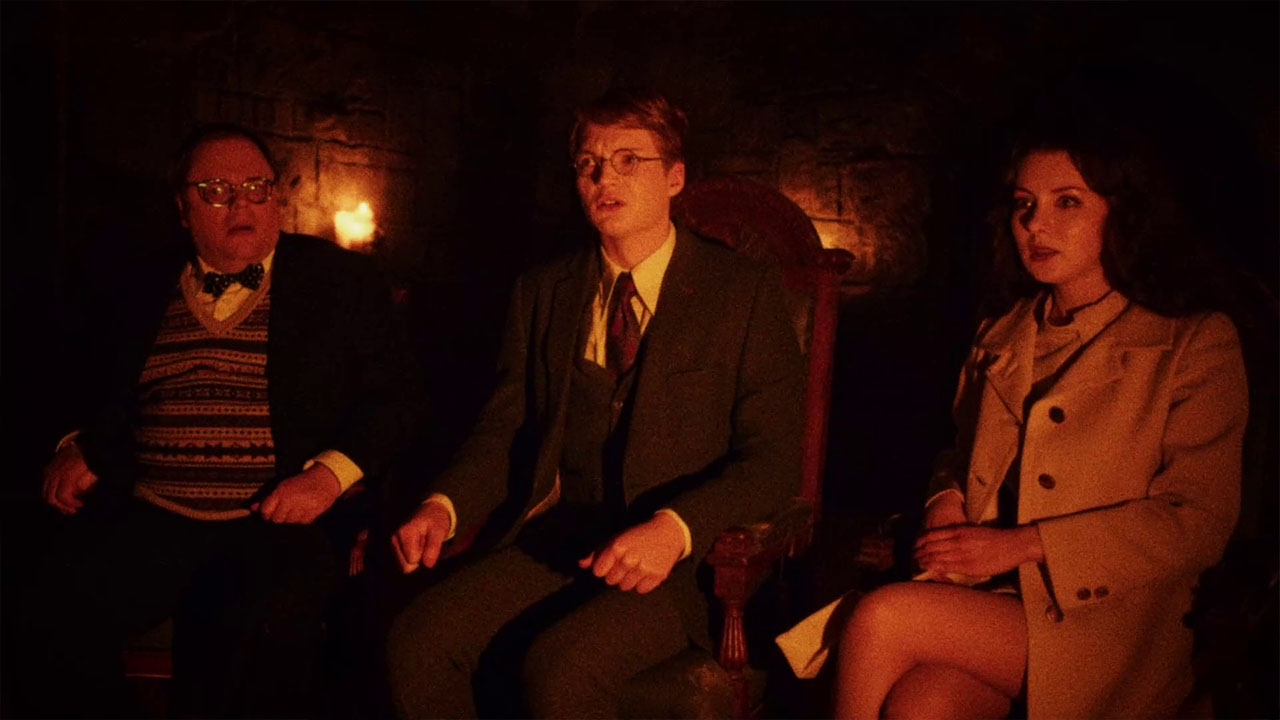 Three visitors sit together in a firelit room in In the Grip of Terror