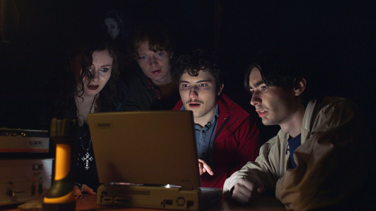 Four investigators gather around a laptop by candlelight in Mr Whispers
